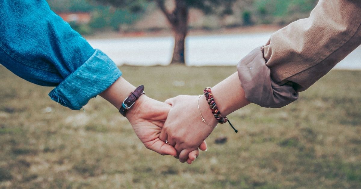 Two female friends holding hands in front of a tree