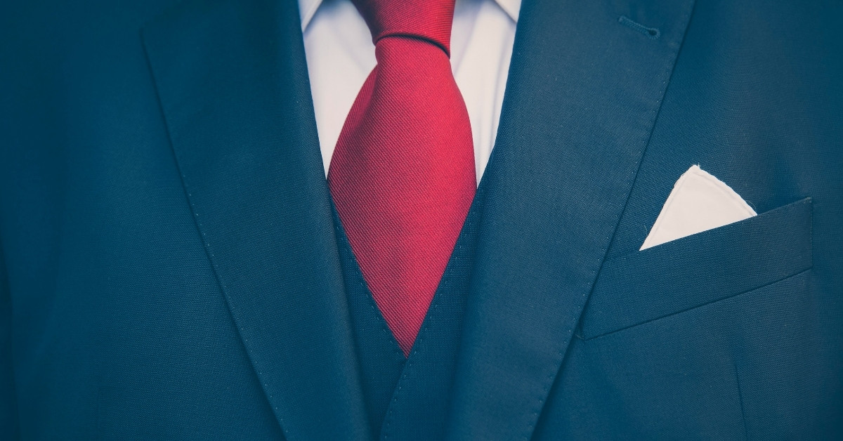 close-up of a person wearing a navy suit with white button shirt, bright red tie, and white pocket square