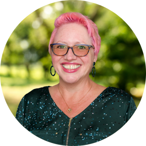 Counselor Angela Shannon with bright pink hair smiles in front of a green nature background