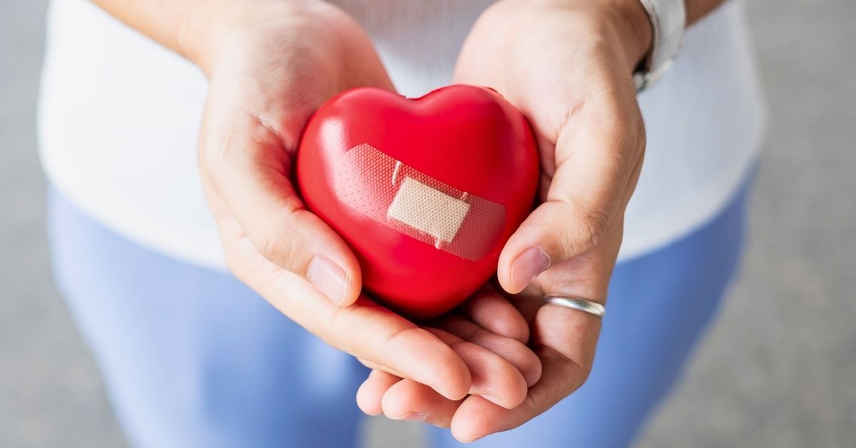 Female hands holding a red heart with a bandaid
