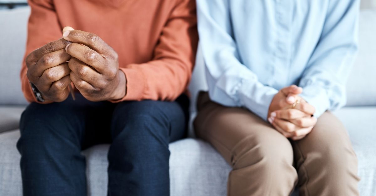 Close-up of couple sitting on couch, slightly apart, with clasped hands, awaiting results