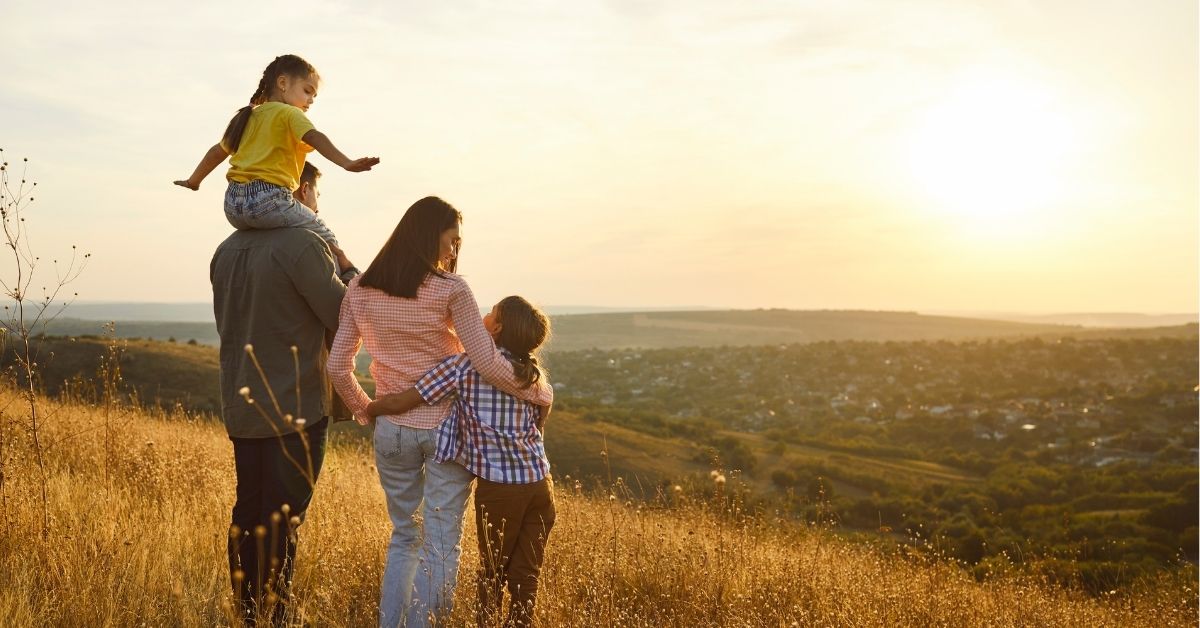 family of two parents and two kids standing in a grassy field looking at sunset