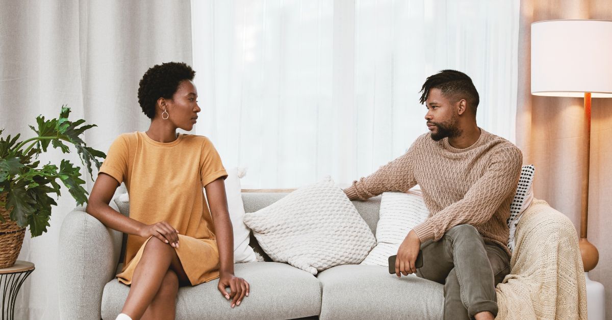 Young black couple sitting separately on opposite ends of a couch, looking at each other