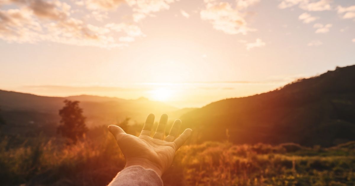 Open hand reaching out toward the sunset or sunrise in the mountains during golden hour
