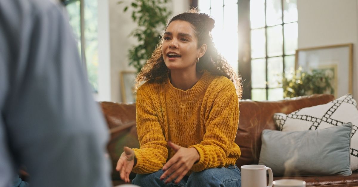 curly-haired young woman wearing yellow sweater talking in therapy session