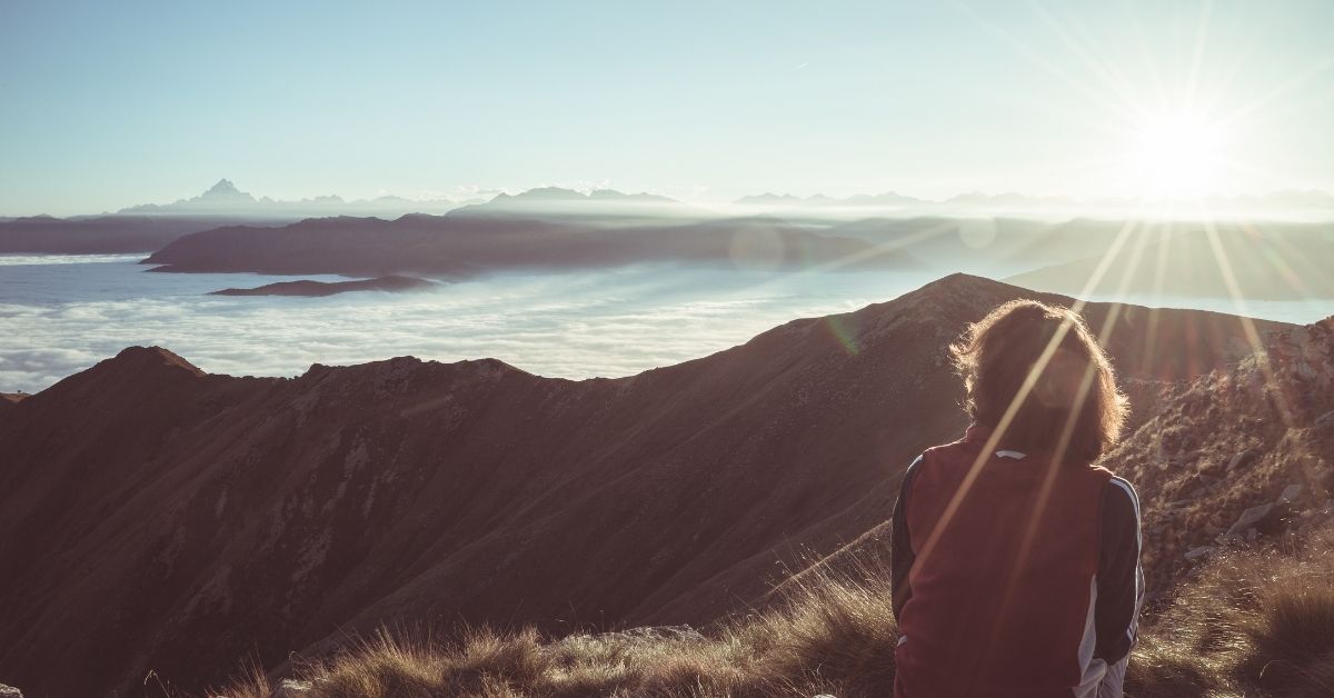 Female hiker reaching her goal at the mountain top and looking at majestic panoramic view of the Alps. Wide angle view at sunset in backlight, toned image, vintage filter, split toning.