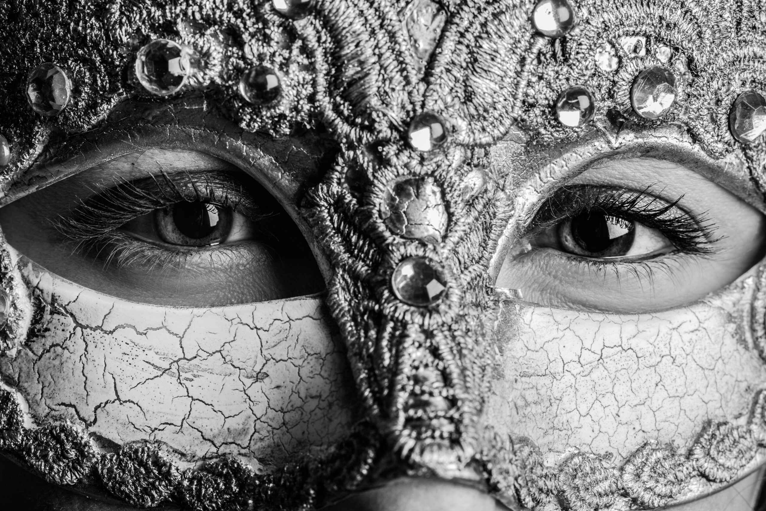 A black and white photo of a woman looking through a decorative mask