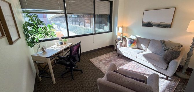 Counseling room with desk, two comfy couches, and large windows with blinds