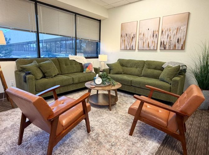 Large corner office room for counseling sessions with several comfy couches, calming decor, and wall with large windows