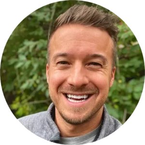 A male counselor smiles warmly while standing in front of a green tree