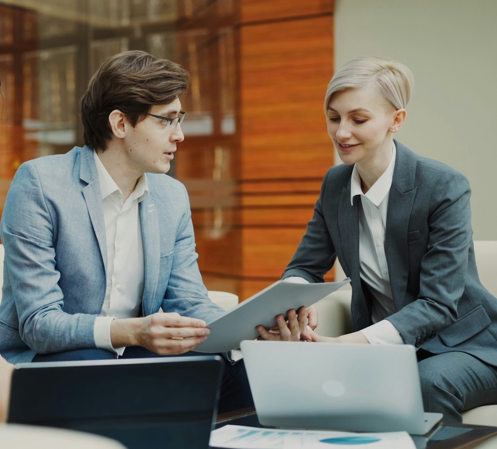 man and woman dressed in suits sitting down for a company meeting