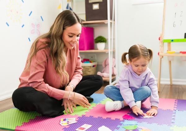 young female counselor sits on floor with elementary-school-aged girl working on a puzzle during play therapy